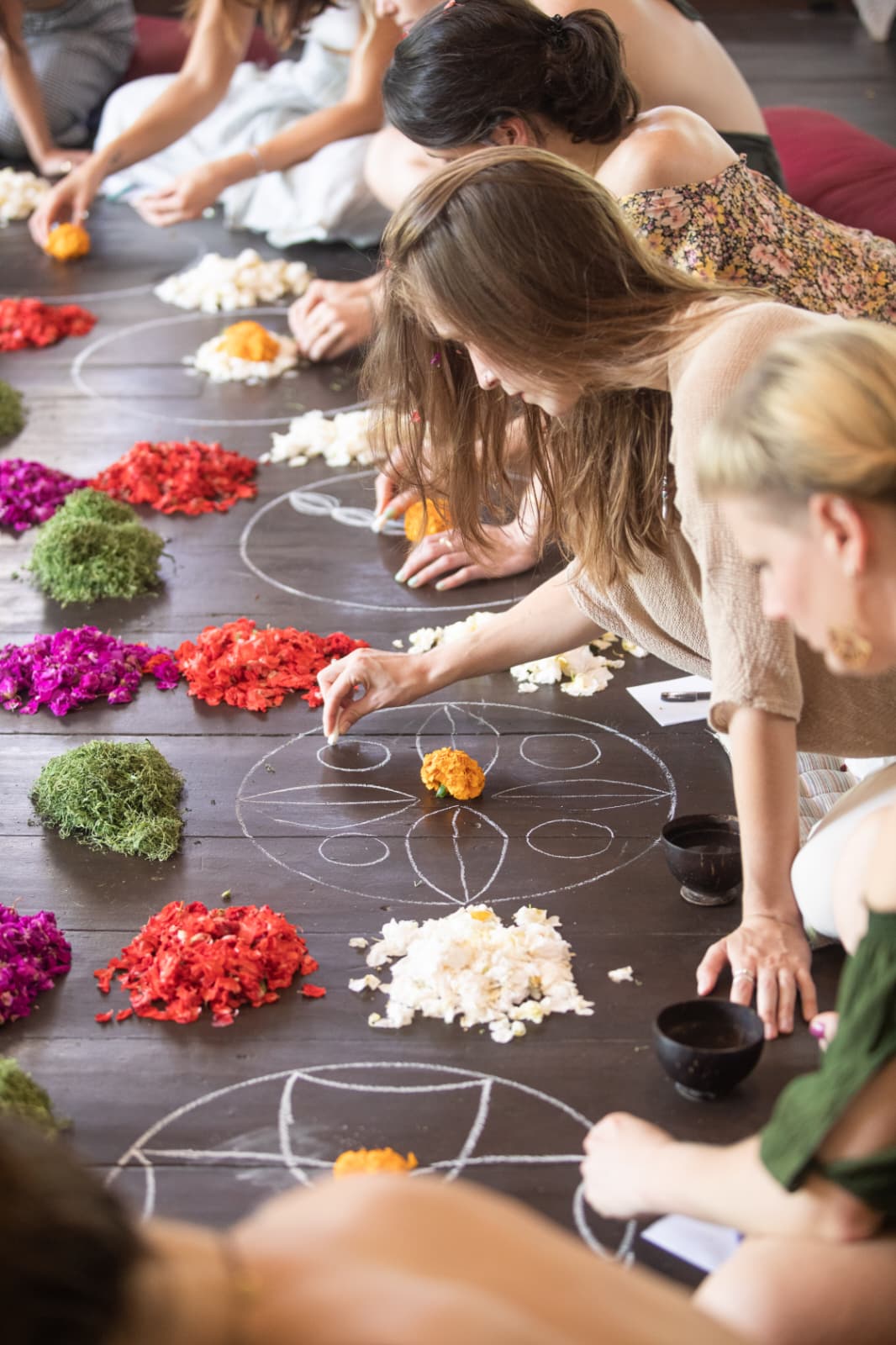 Students laying petals into a chalk mandala on a dark timber floor